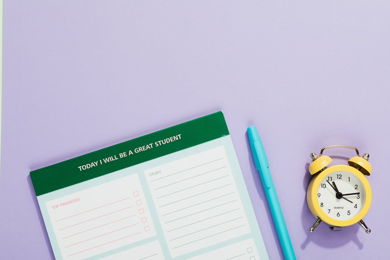 who-we-are A vibrant still life with a motivational student planner, pen, and yellow alarm clock on a pastel backdrop.