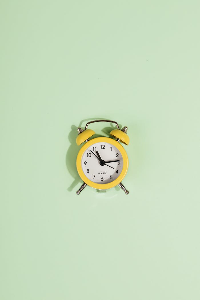 services-03 Yellow analogue alarm clock on a pastel green backdrop, perfect for concepts of time and minimalism.