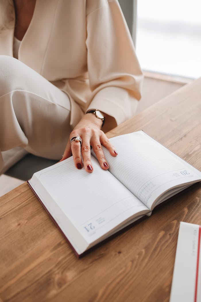 story-01 Close-up of a woman's hand on an open diary on a wooden table, capturing an intimate reading moment indoors.