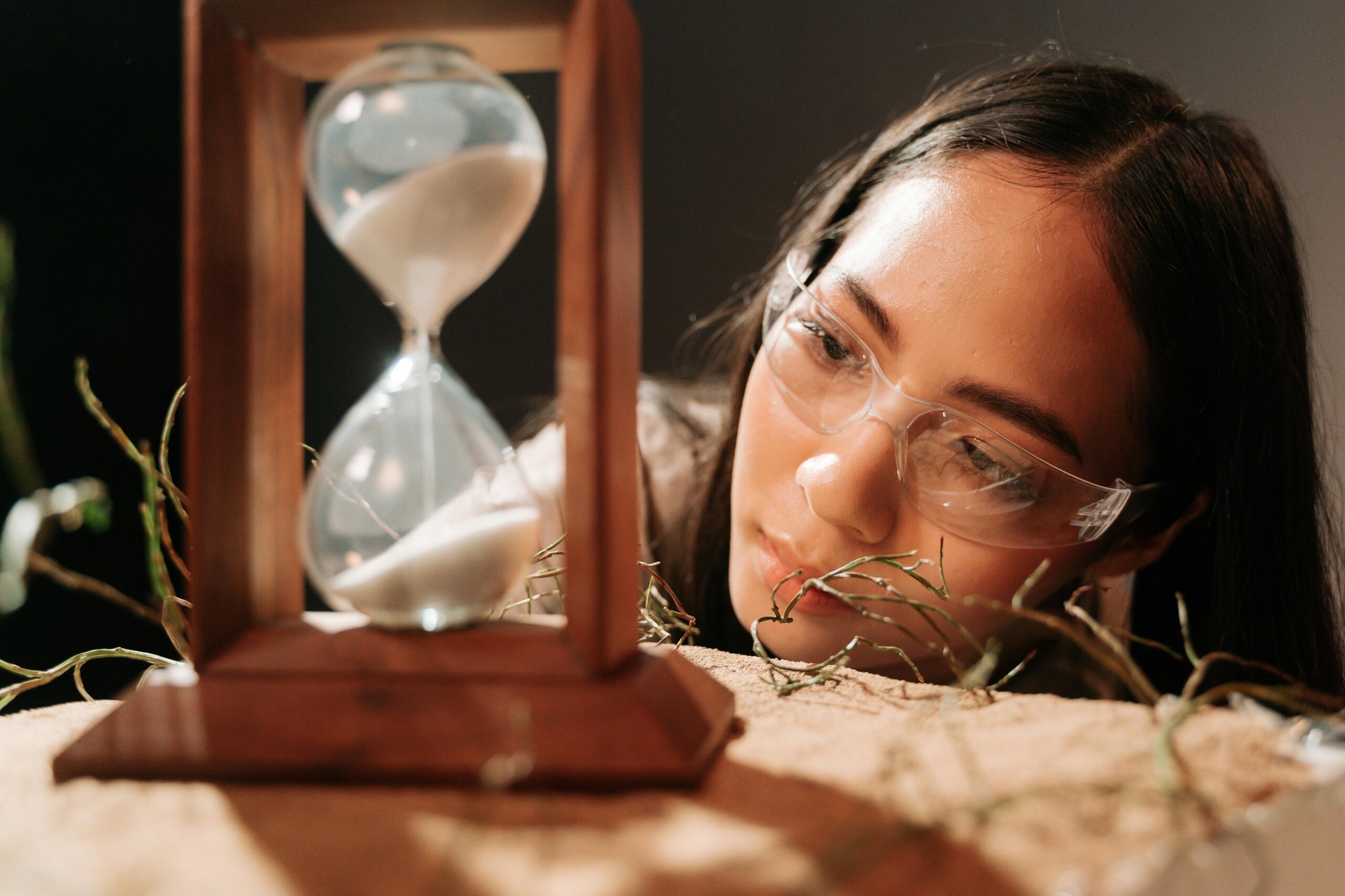 Keskendu Positiivsele: Mõtete Eesmärgistamine A woman wearing glasses observes an hourglass, symbolizing time and reflection.